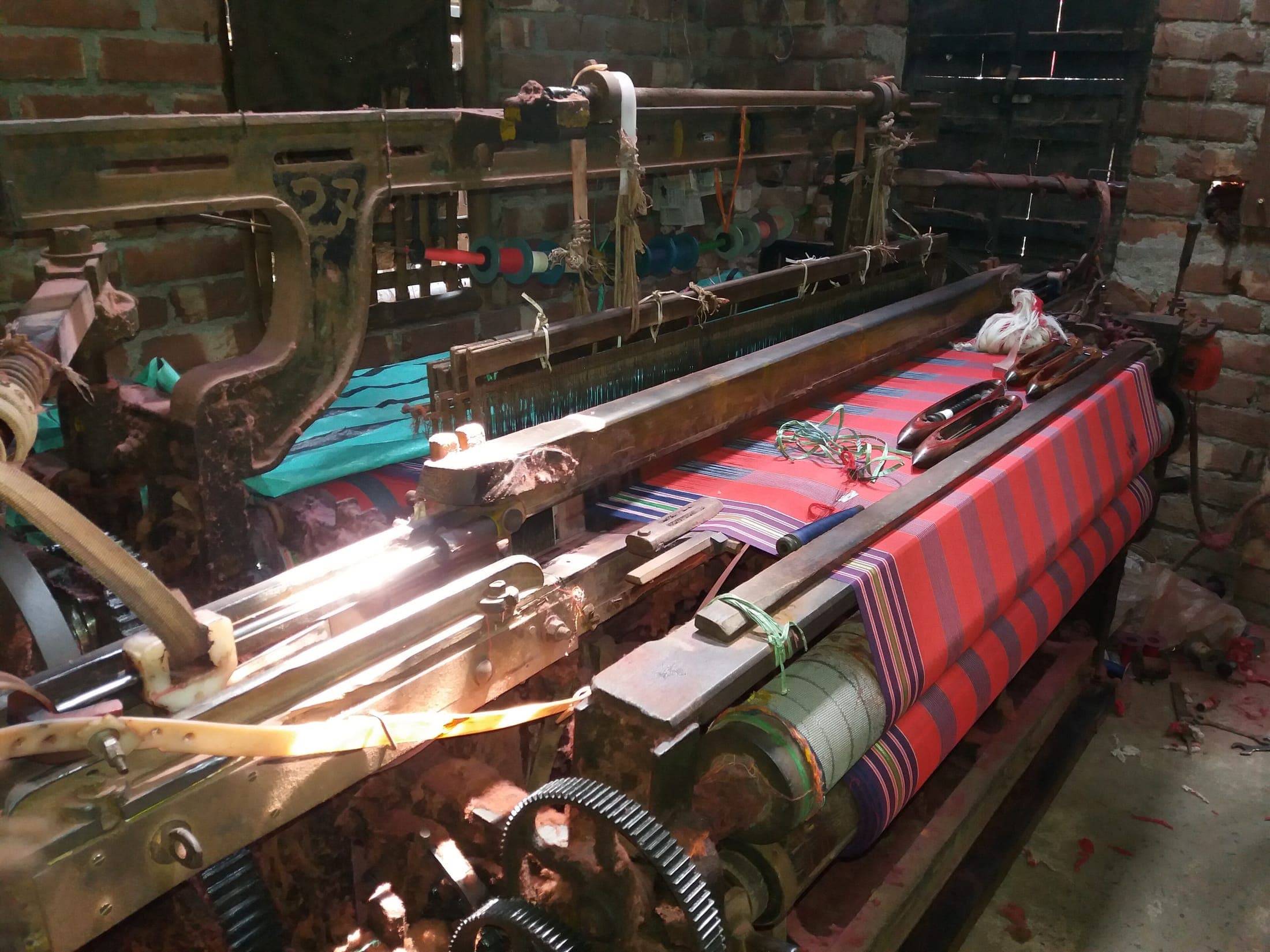 A power loom weaving striped fabric, with the warp running back to the beam